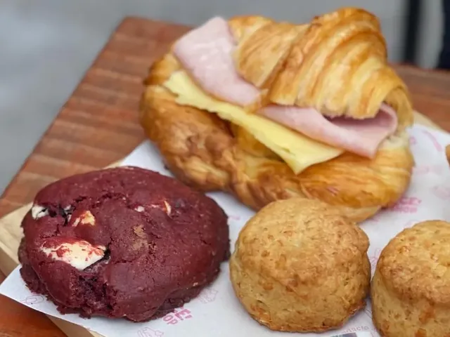 Tabla de madera con un croissant de jamón y queso, scones y una galleta red velvet