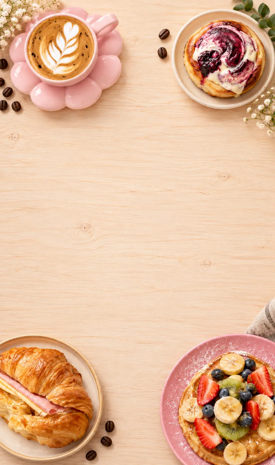 Mesa de madera clara vista desde arriba con un café con latte art en taza rosa, un croissant de jamón y queso, un rol con arándanos y un panqueque con frutas